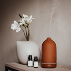 a vase with a flower and two bottles of essential oils on a table