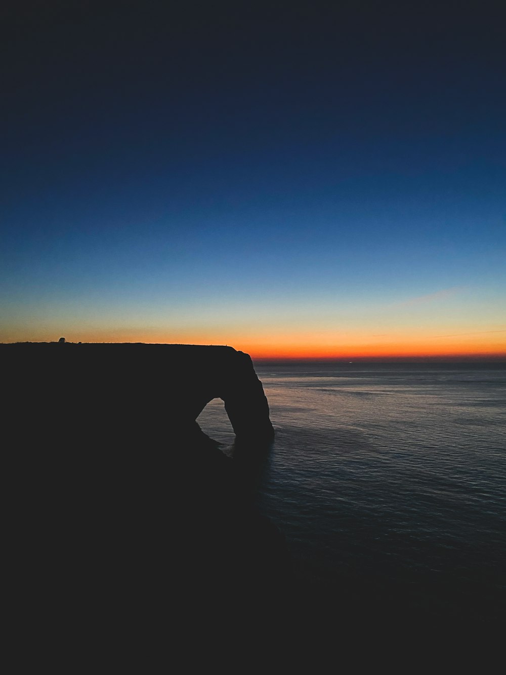 the sun is setting over the ocean with a rock formation in the foreground