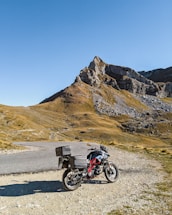 A scenic view of a motorcycle and 4x4 parked beside a winding mountain road under a clear blue sky.