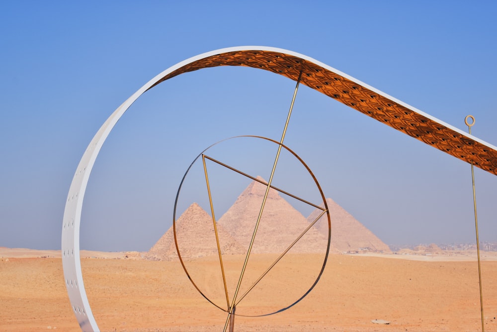 a sculpture in the middle of a desert with two pyramids in the background