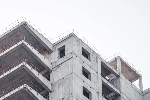 Industrial concrete factory with workers assembling premolded structures under a cloudy sky.