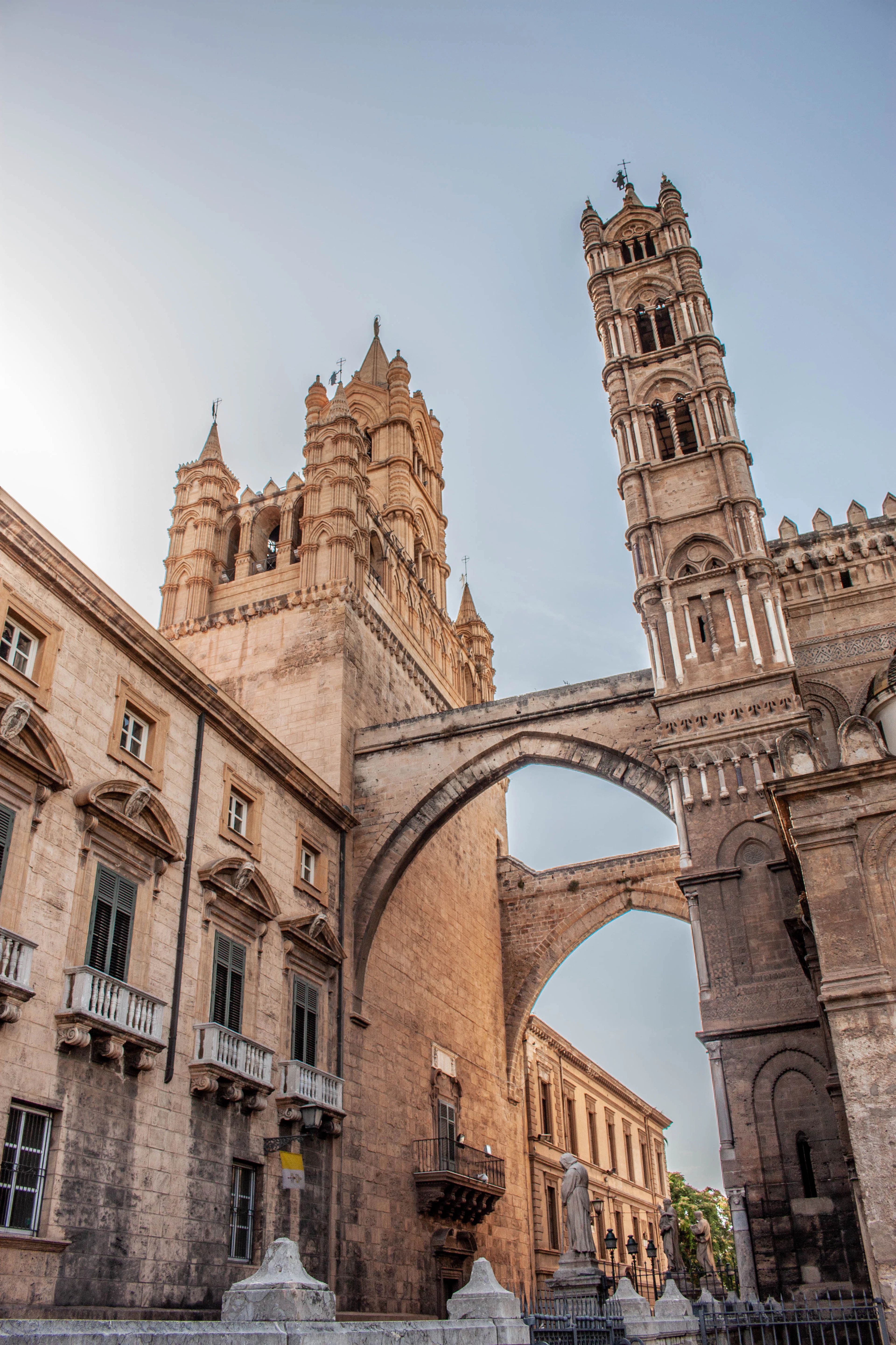 Palermo Cathedral's Gothic towers linked by a stone arch bridge, glowing in late afternoon light.