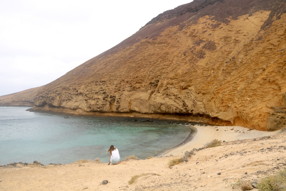 a woman standing on a beach next to a cliff