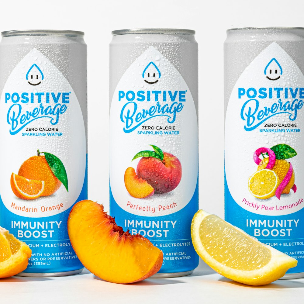 three cans of positive beverage with oranges and lemons