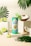 A turquoise and green energy drink can labeled 'Positive Energy' stands on a white platform. It is surrounded by fresh coconut halves and lime slices, with tropical palm leaves adding to the vibrant, tropical theme. A small green and white paper umbrella is placed inside a coconut half, enhancing the tropical atmosphere.