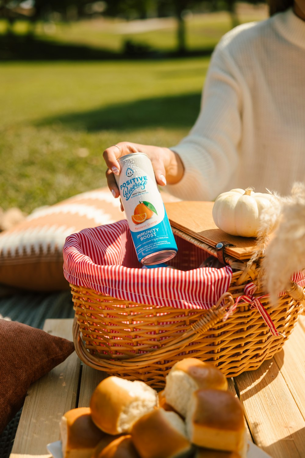 a person sitting at a picnic table with a basket of bread and a bottle of