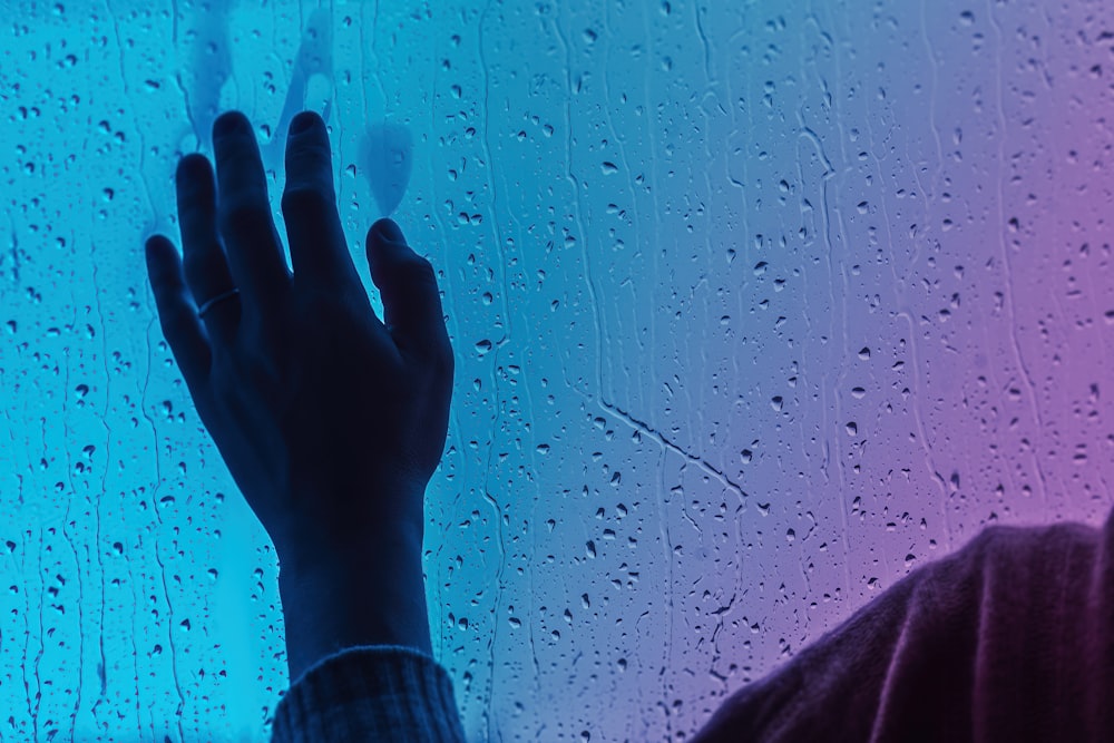 a person standing in front of a window covered in rain