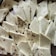 Several pieces of a white, porous snack have been cut into irregular shapes and arranged on a surface. Some pieces are plain, while others are speckled with what looks like small black seasoning or peppercorns.