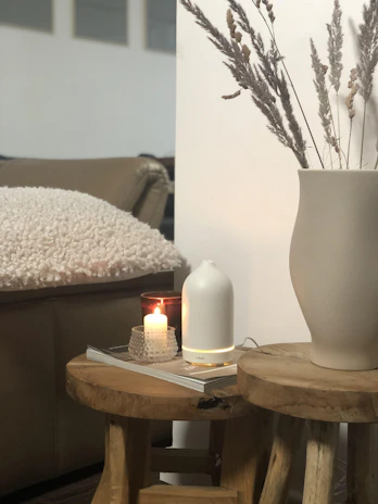 A cozy living room scene featuring auramūza diffuser stones arranged on a wooden tray beside a flickering candle.