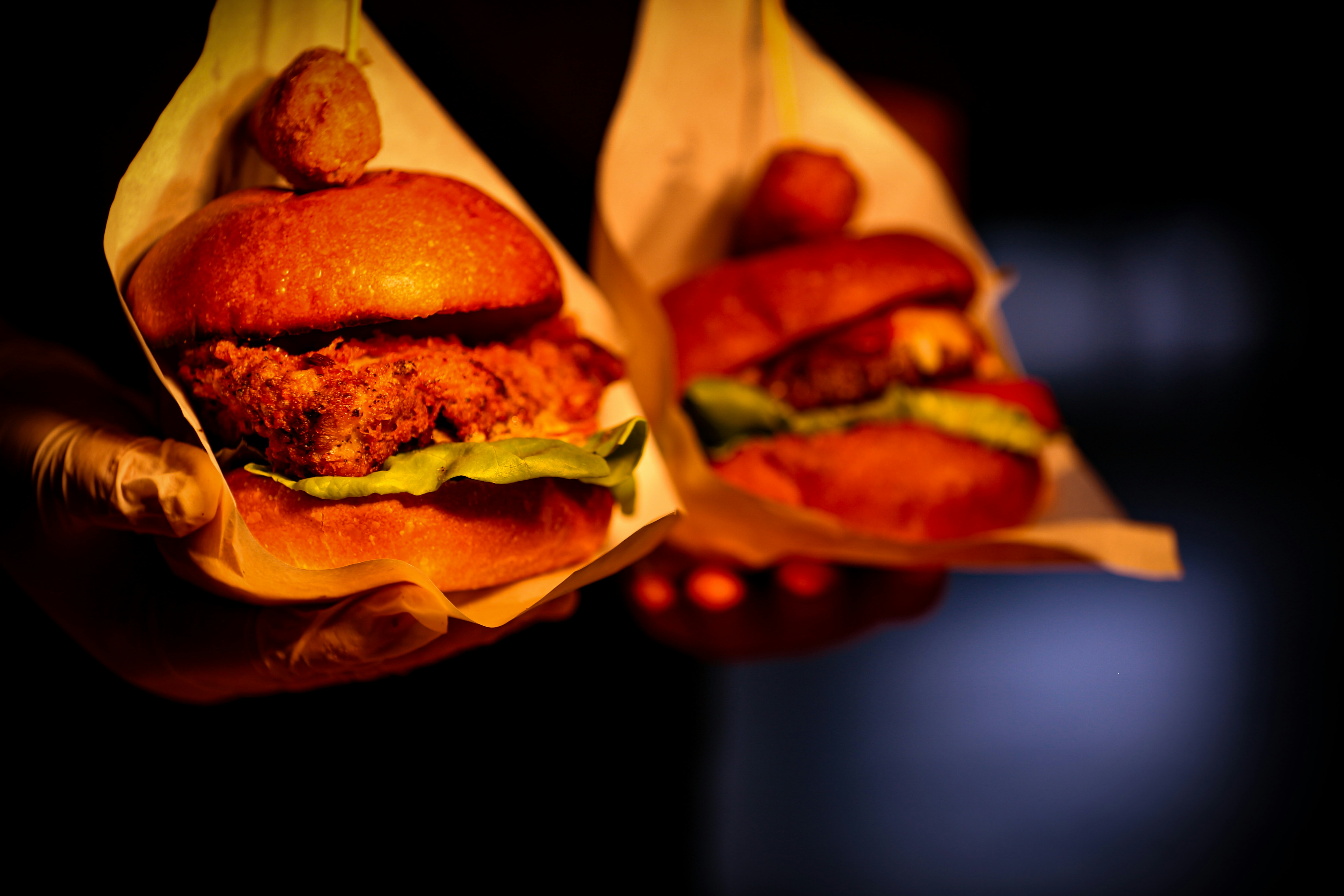 Hands holding two chicken burgers in the dark