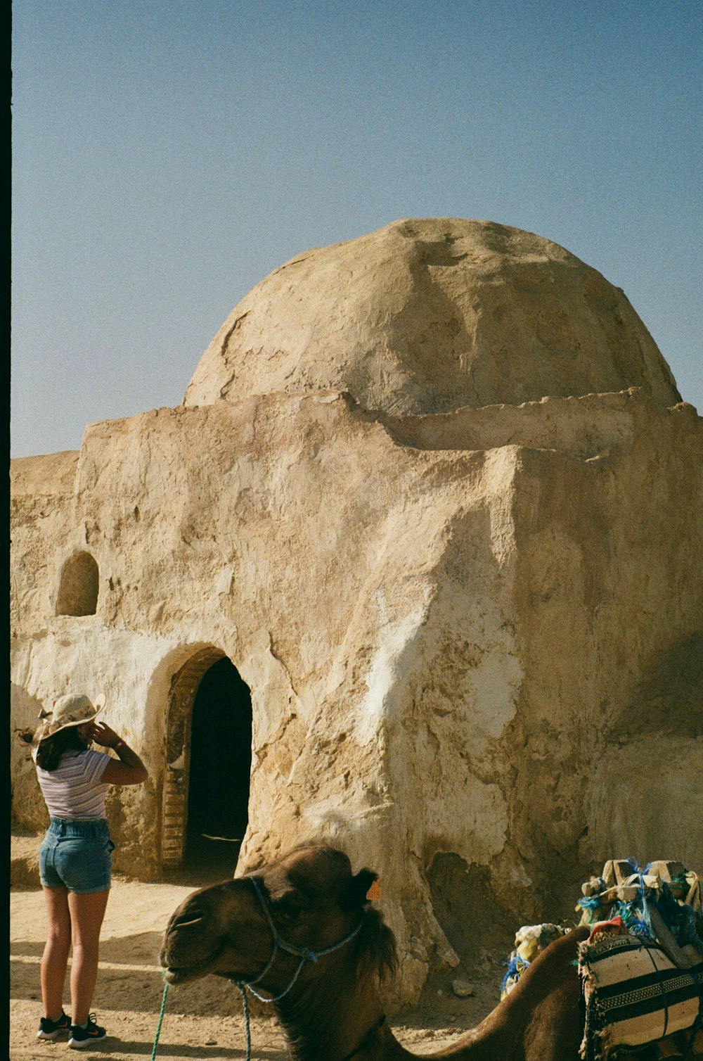 a woman standing next to a camel in front of a rock structure