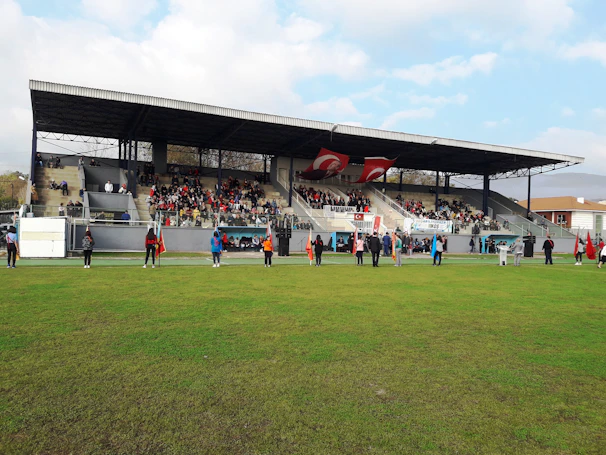 The opening ceremony with players, coaches, and families gathered on the field, waving flags and cheering under a bright blue sky.