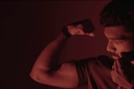 Close-up of a client’s muscular arm mid-curl, veins visible, with sweat glistening under gym lights.