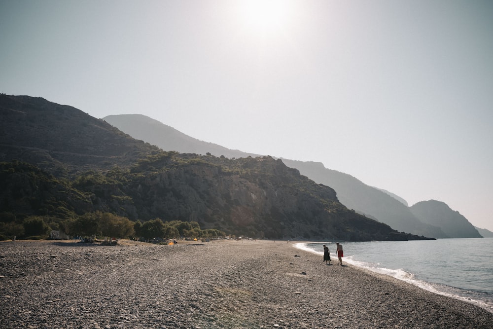 a couple of people standing on top of a sandy beach