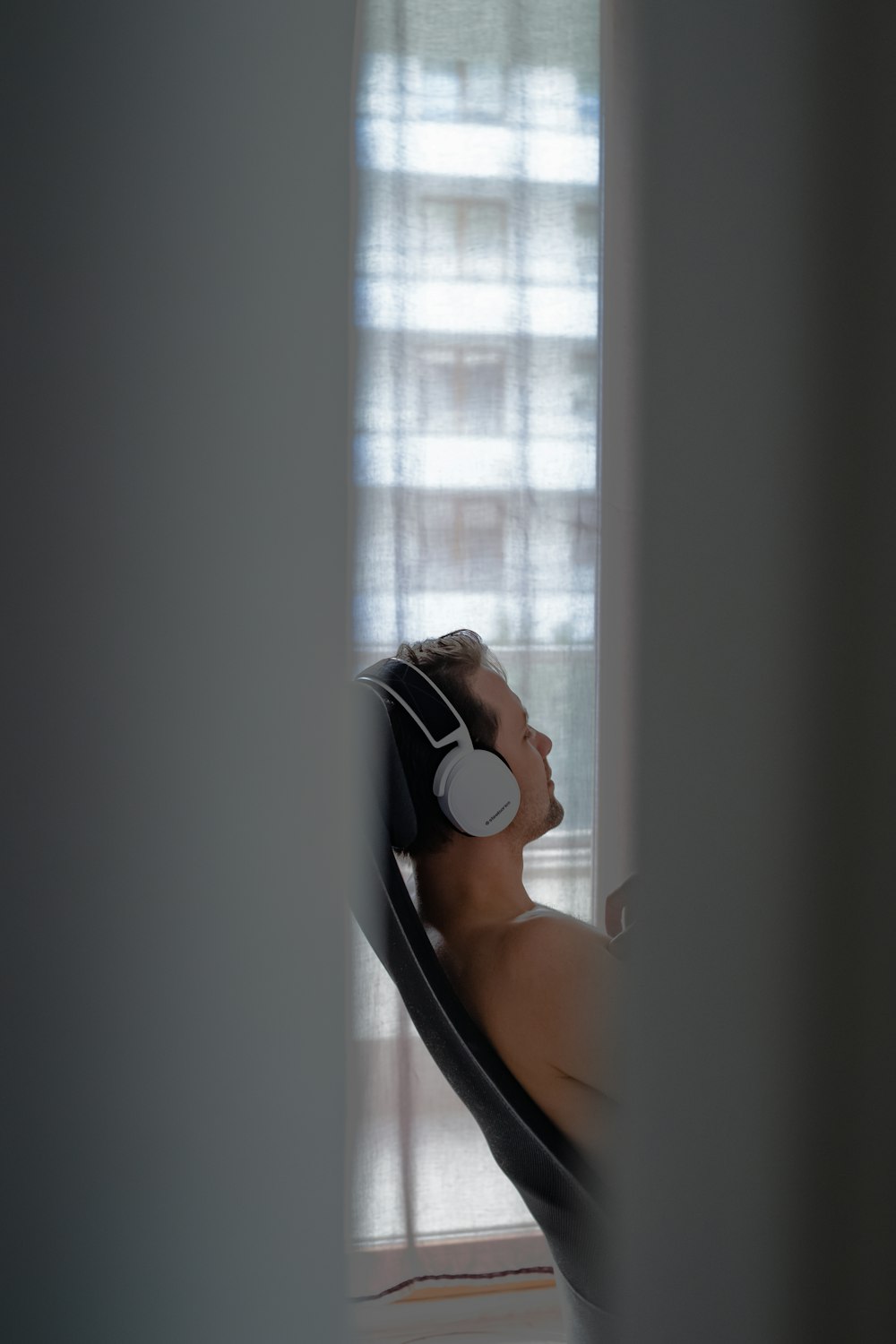 a shirtless man wearing headphones looking out a window