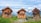 Three rustic wooden cabins are set against a backdrop of majestic mountains under a partly cloudy sky. These cabins are surrounded by lush green grass and a wooden fence. The windows of the cabins are adorned with colorful flowers, and there are several chairs outside, suggesting a cozy and inviting atmosphere.