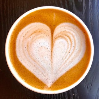 A creamy latte art heart drawn on a smooth foam surface in a cozy café setting.