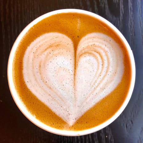 A creamy latte art heart drawn on a smooth foam surface in a cozy café setting.