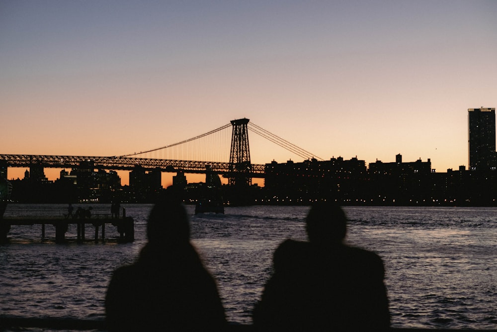 two people sitting on a bench looking at a bridge