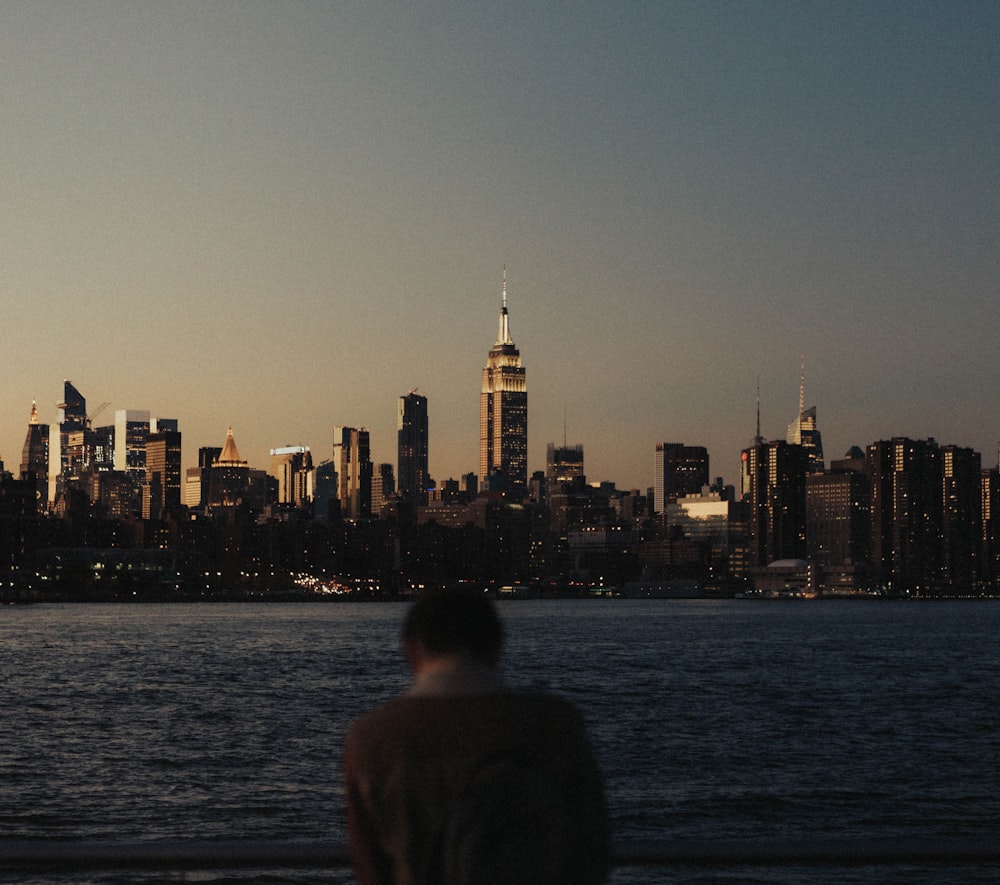 a man standing in front of a body of water with a city in the background