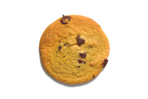 Close-up of a golden-baked American cookie with visible chocolate chunks on a minimalist white plate.