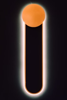 A minimalistic design featuring a vertical black bar with a rounded top, outlined by a soft glow. The top of the bar is capped with a glowing orange circle, creating a striking contrast against the dark background.