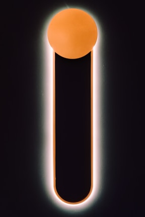 A minimalistic design featuring a vertical black bar with a rounded top, outlined by a soft glow. The top of the bar is capped with a glowing orange circle, creating a striking contrast against the dark background.