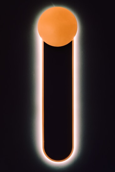 A minimalistic design featuring a vertical black bar with a rounded top, outlined by a soft glow. The top of the bar is capped with a glowing orange circle, creating a striking contrast against the dark background.