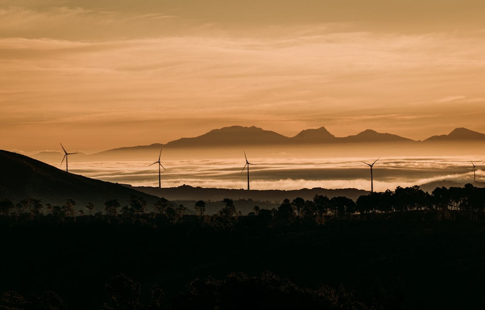a sunset view of a mountain range with wind mills in the foreground