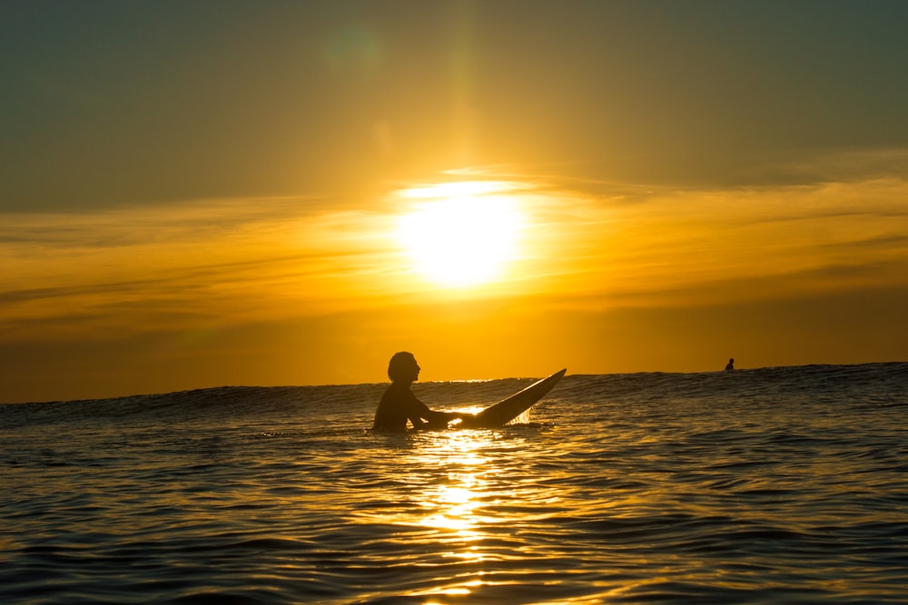 a person sitting on a surfboard in the ocean at sunset