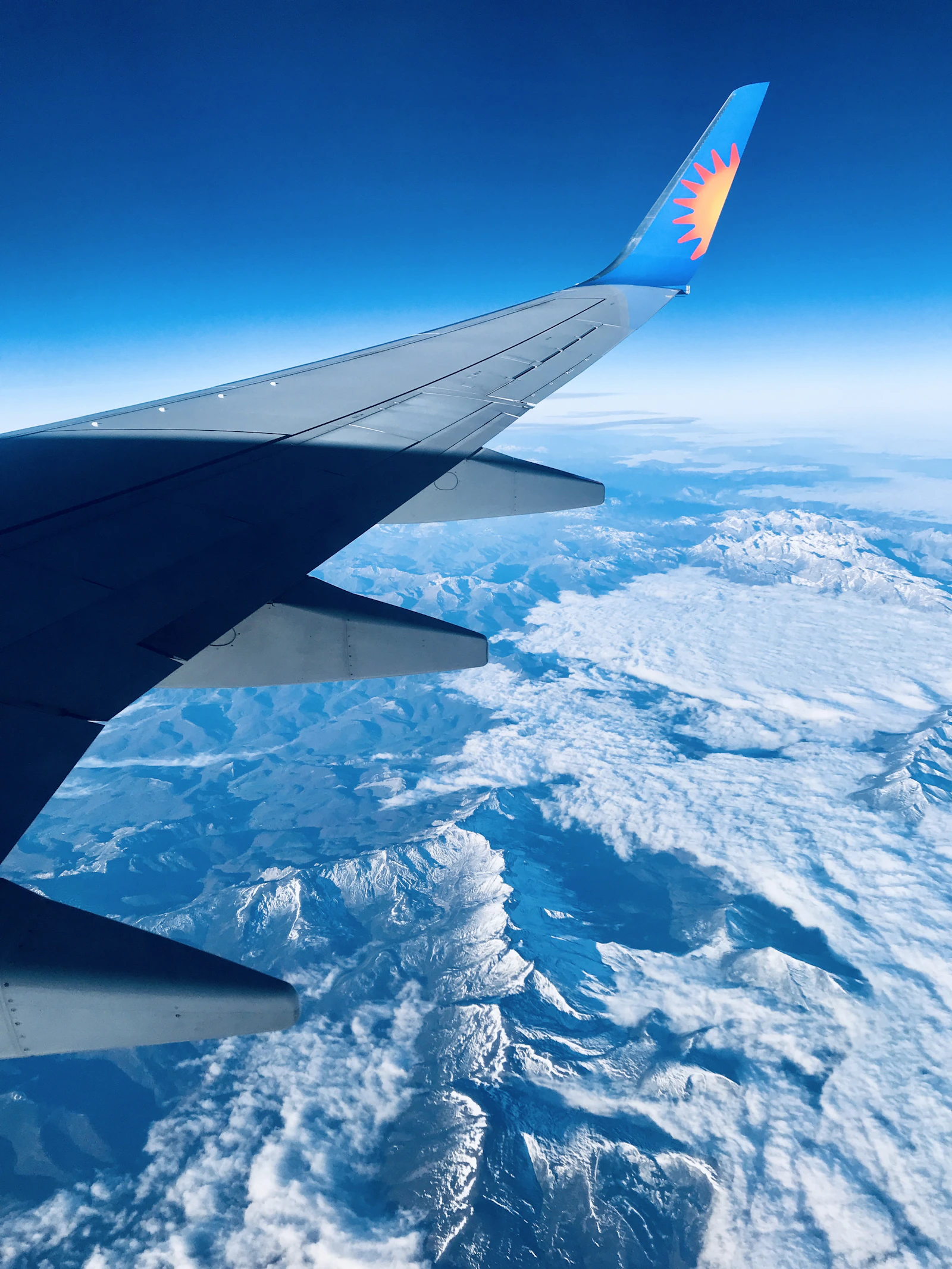 An aircraft wing above a mountain range, the route between a brand and the people it wants to reach