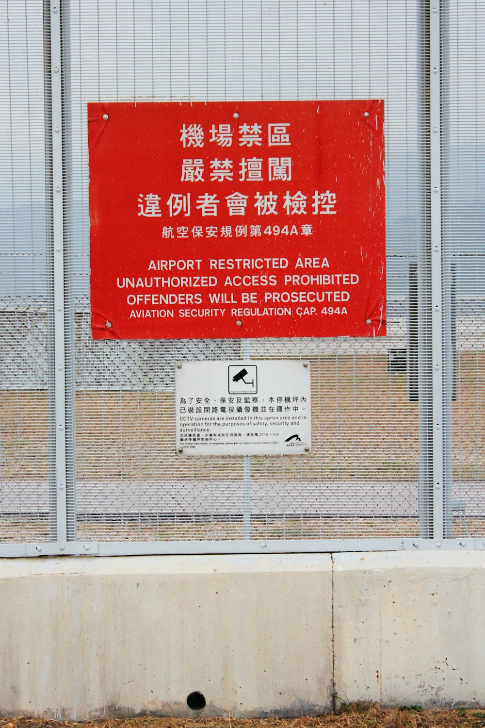 a red sign on a fence that says airport restricted area unauthorized access prohibited