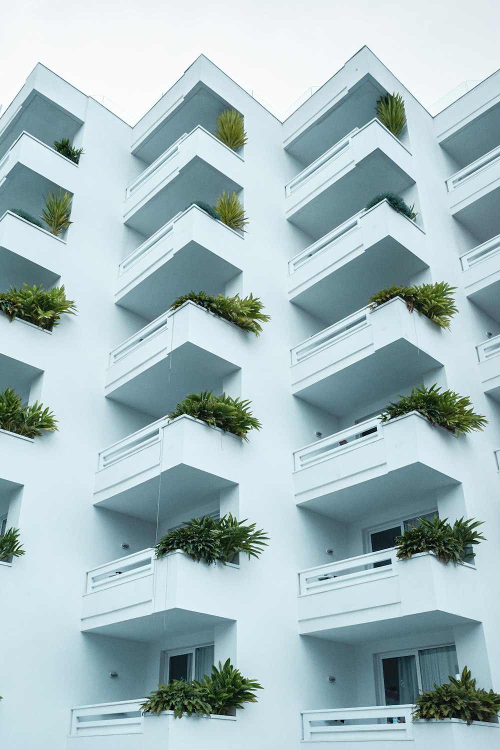 a tall white building with balconies and plants on the balconies