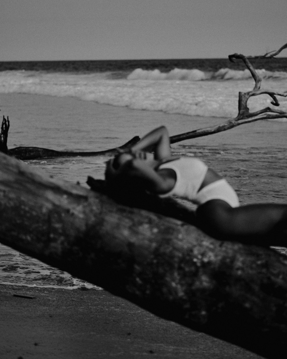 a black and white photo of a woman laying on a log
