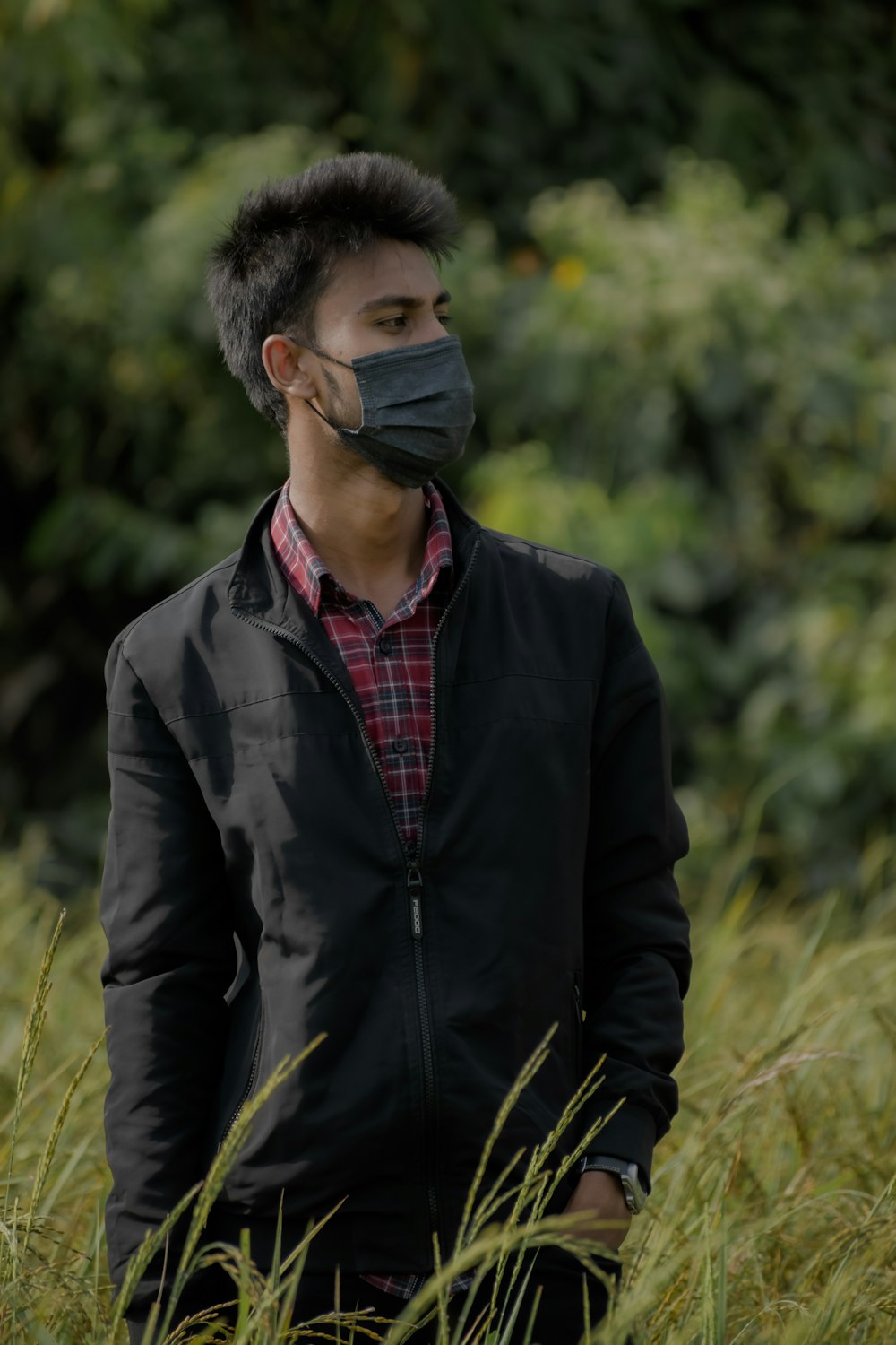 a man wearing a face mask standing in tall grass