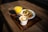 A breakfast setting with a cup of cappuccino featuring latte art, a small glass of orange juice, and a plate containing scrambled eggs with herbs, toast, and toast with what appears to be apricot jam, all placed on a wooden serving tray on a wooden table.