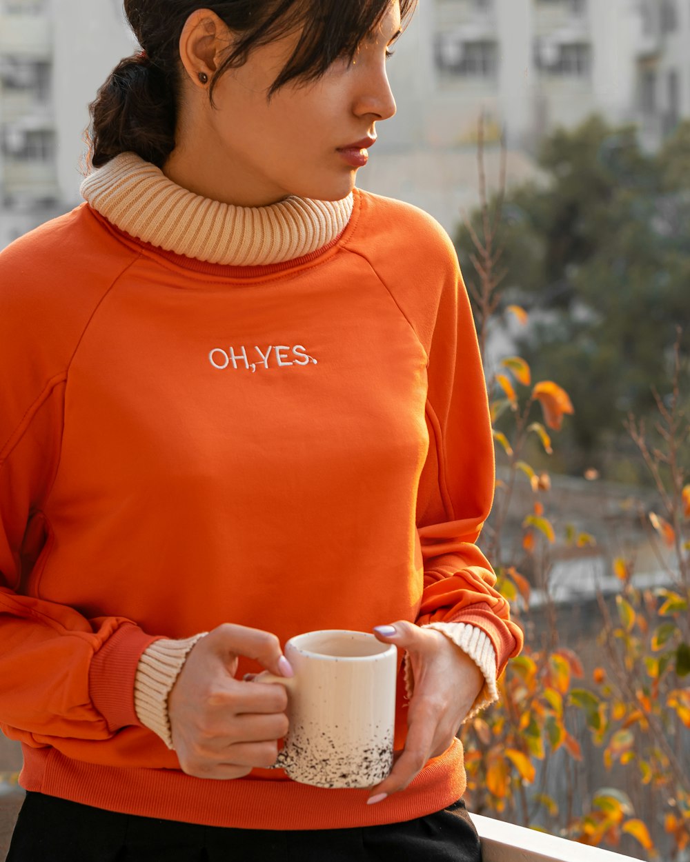 a woman in an orange sweater holding a coffee cup