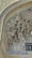 Intricate Islamic architectural tile work featuring elaborate geometric patterns and Arabic calligraphy. The mosaic is primarily composed of blues, golds, and whites, creating a rich tapestry of colors. The arch under which this design is placed is finely adorned, demonstrating traditional artistry.