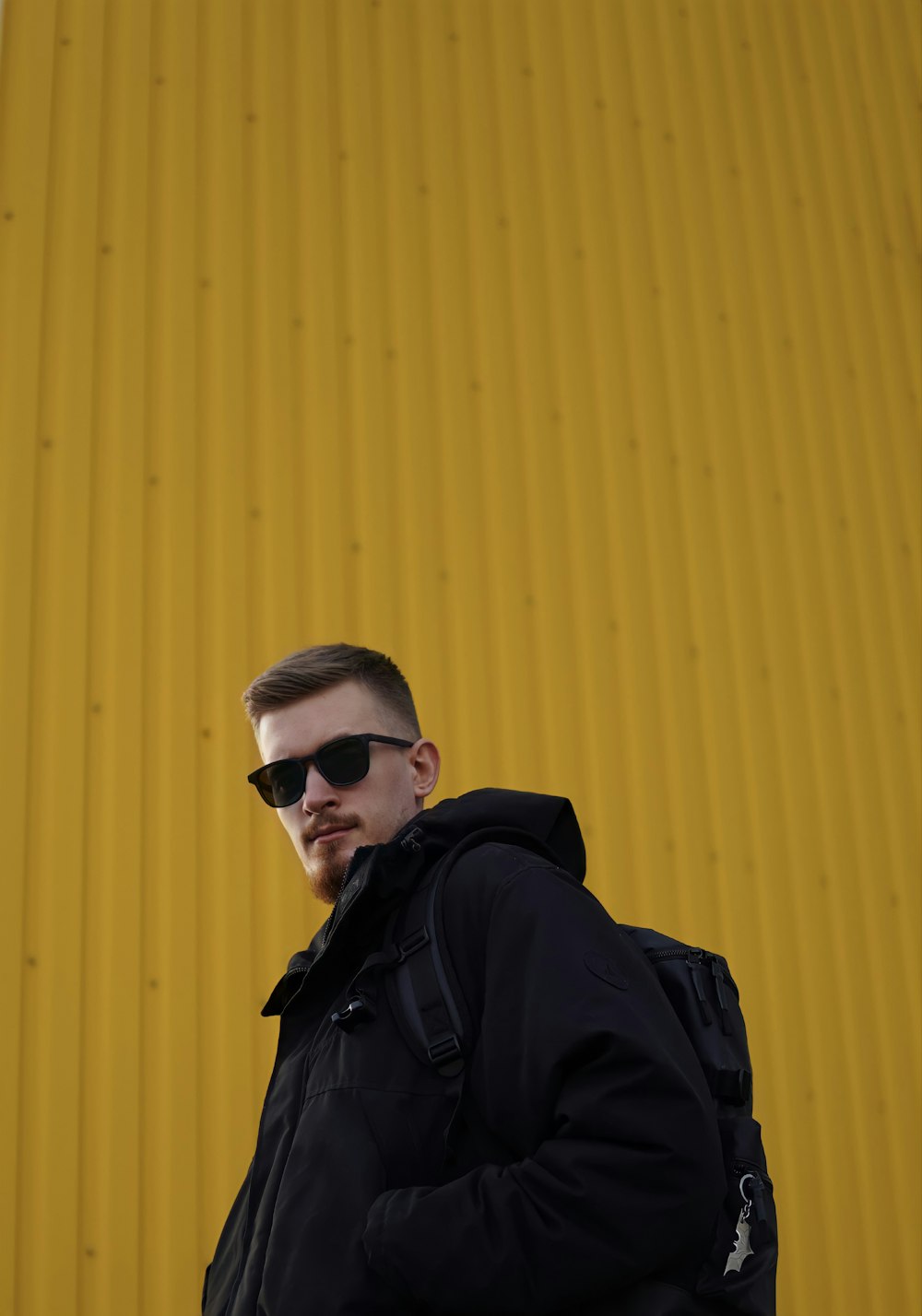 a man in a black jacket and sunglasses standing in front of a yellow wall