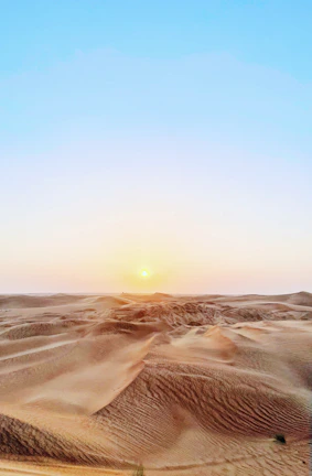 Golden desert dunes under a vast, clear sky at sunset.