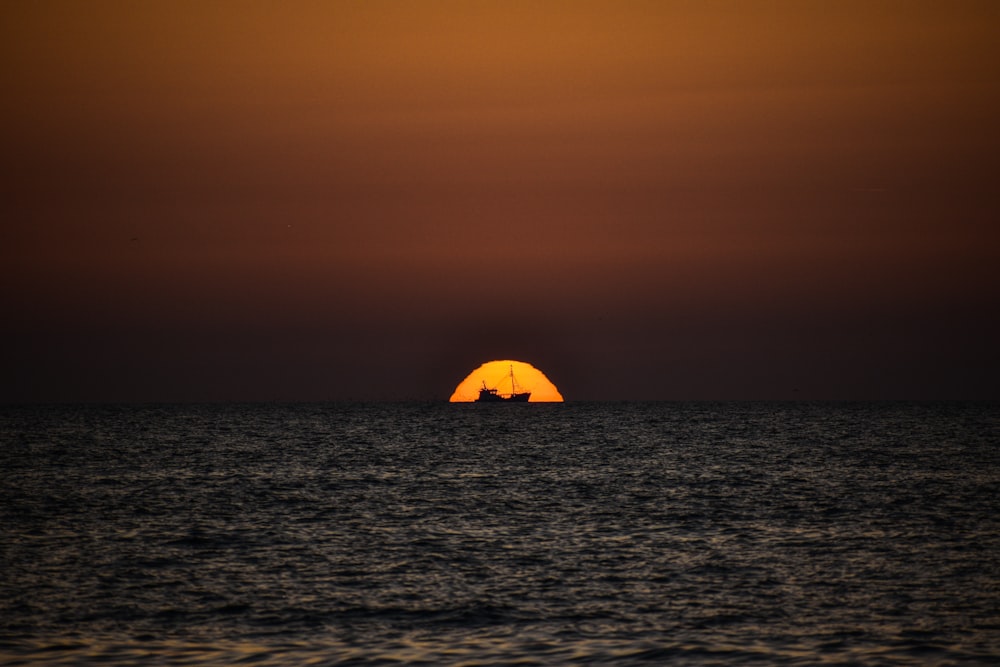 o sol está se pondo sobre o oceano com um barco à distância