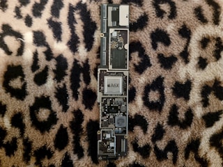 A computer motherboard with visible electronic components including a central A6X chip. The motherboard is positioned on a leopard print fabric background.
