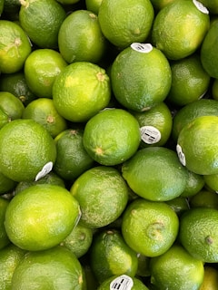 A pile of fresh, green limes with stickers on some of the fruits, indicating they are commercially processed for sale.