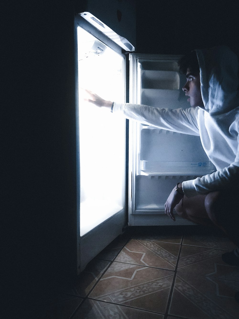 Eine Person in einem Kapuzenpulli, die in einen offenen Kühlschrank greift