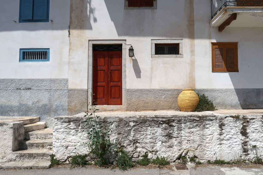 a white building with a red door and a yellow vase