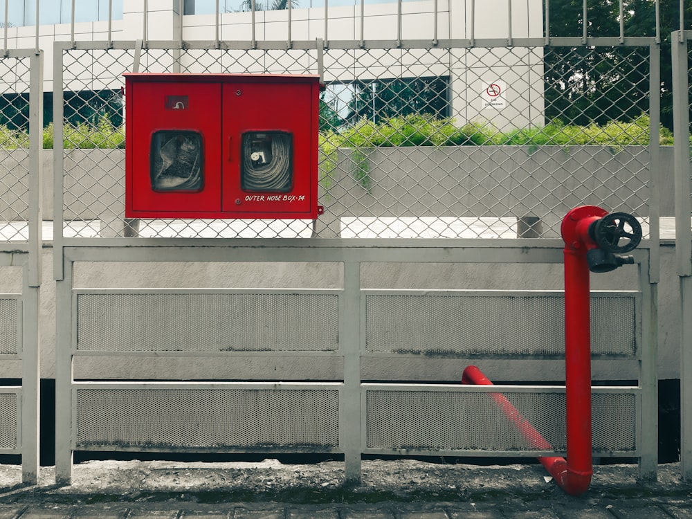 Ein roter Hydrant sitzt neben einem Metallzaun