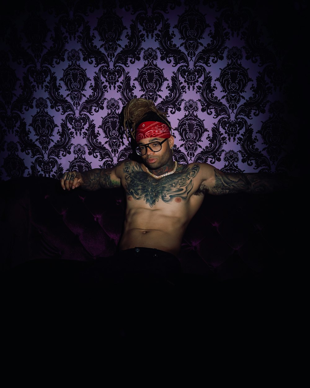 a shirtless man with a bandana on sitting on a couch