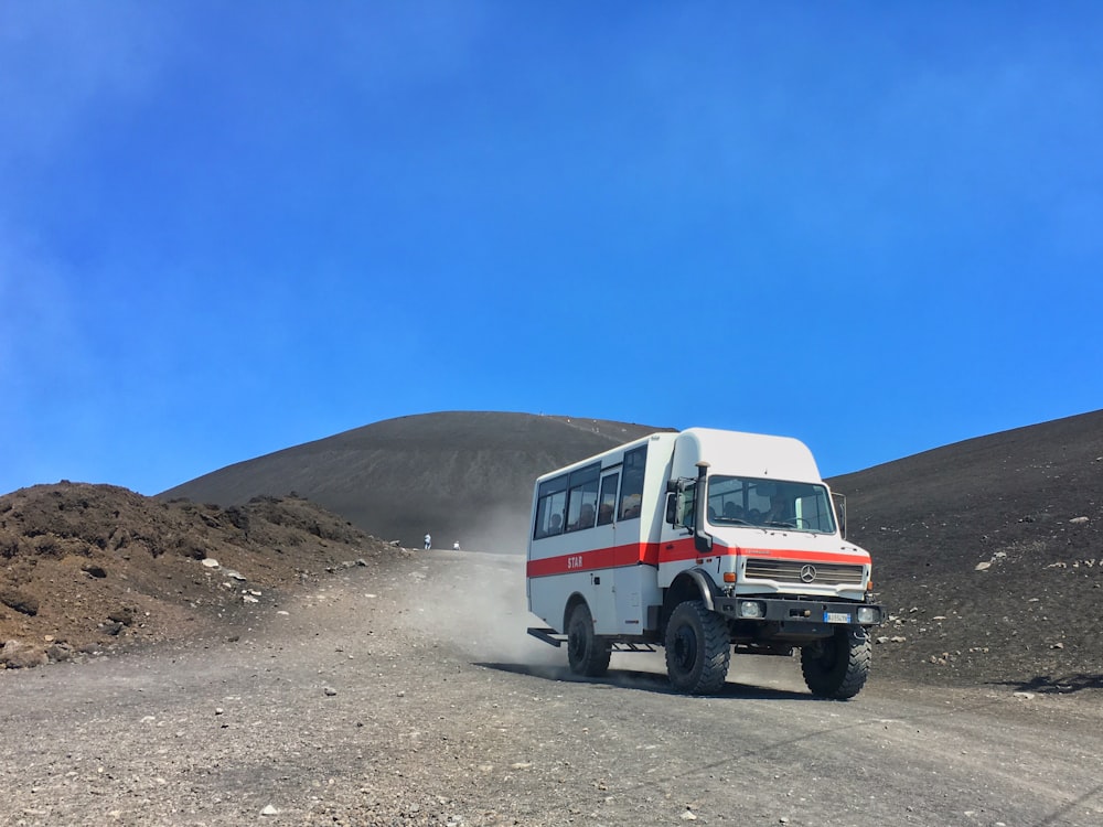 a white and red bus driving down a dirt road