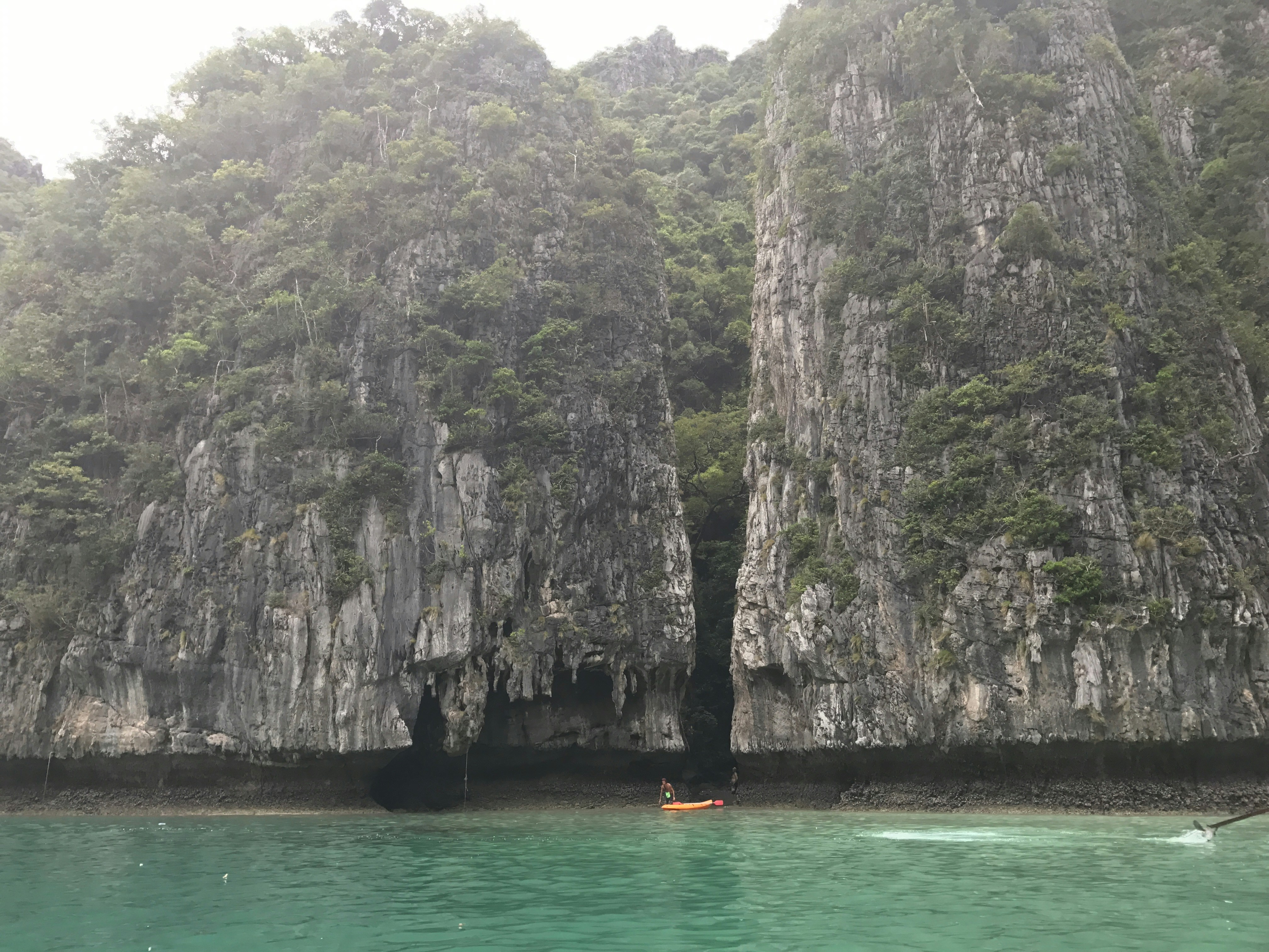 Person kayaking in calm turquoise coastal waters near rocky cliffs, sunny day, adventure sport