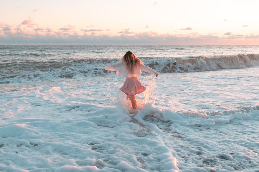 a woman in a pink dress walking into the ocean